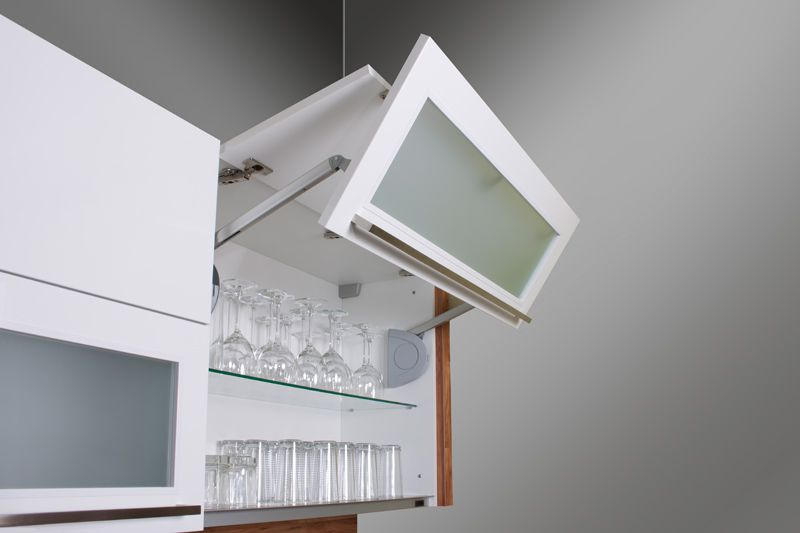 Faltbeschlag Weißer Hängeschrank mit hochgeklappter Tür, darin stehen Weingläser und Trinkgläser auf Glasböden.